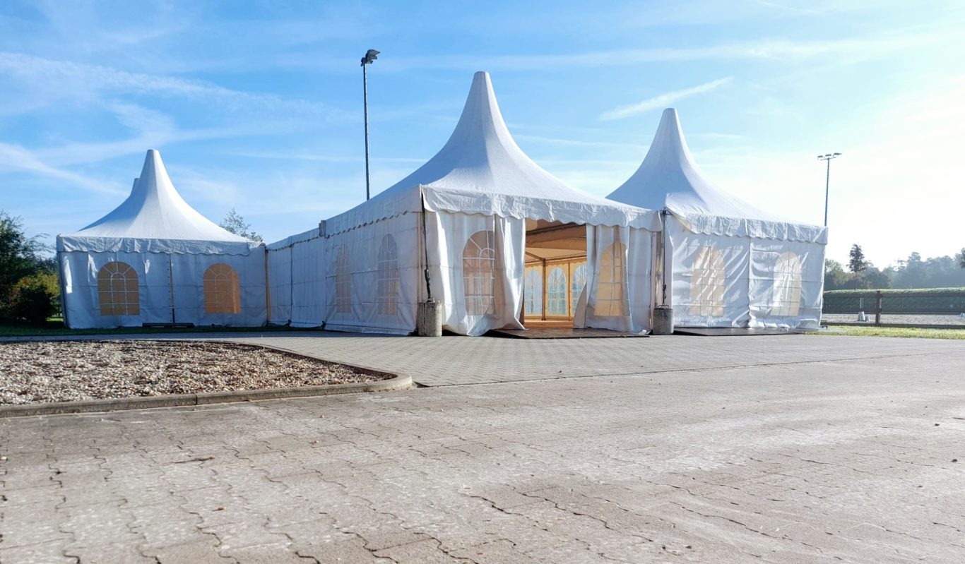 Pagodenzelte mit Zelt im Verbund Helle Zelte mit Spitzen, auf einem befestigten Platz unter blauem Himmel.