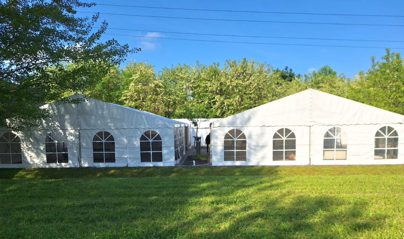 zwei 10m breite Zelte auf einer Wiese Zwei große Zelte mit Fenstern stehen auf einer Wiese umgeben von Bäumen.