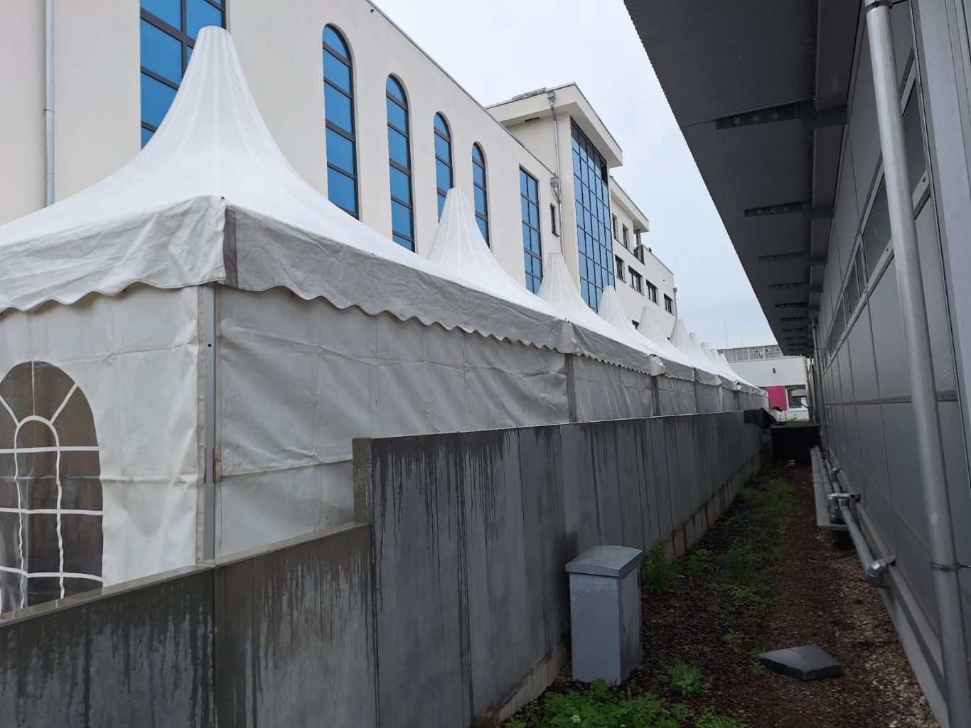 Viele Pagodenzelte aneinandergereiht Zeltreihe entlang einer Wand, grauer Himmel im Hintergrund.