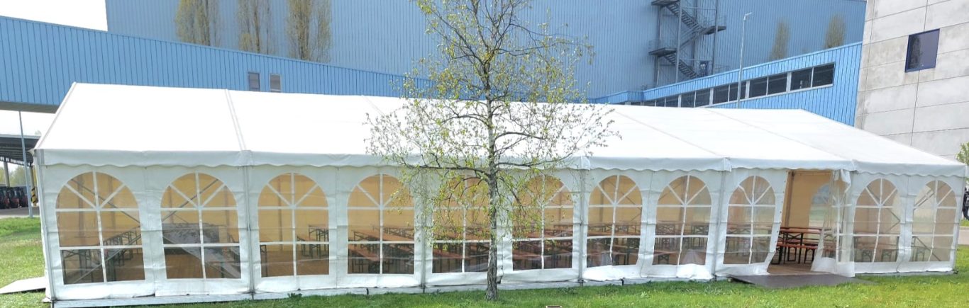 Festzelt mit Seitenfenstern Ein weißes Zelt mit großen Fenstern, umgeben von Gras.