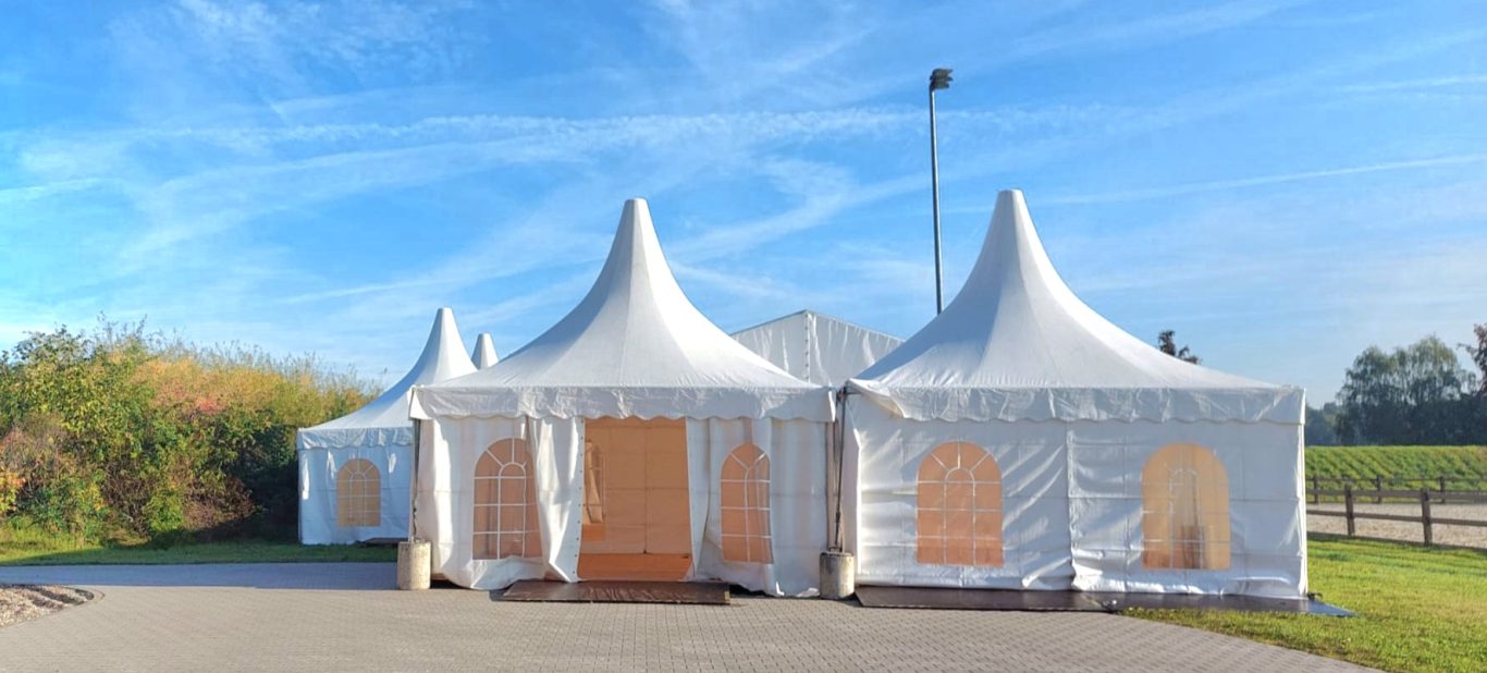 Pagoden und Zelt im Verbund auf Reiterhof Zelt mit spitzen Dächern, umgeben von grünen Wiesen und blauem Himmel.