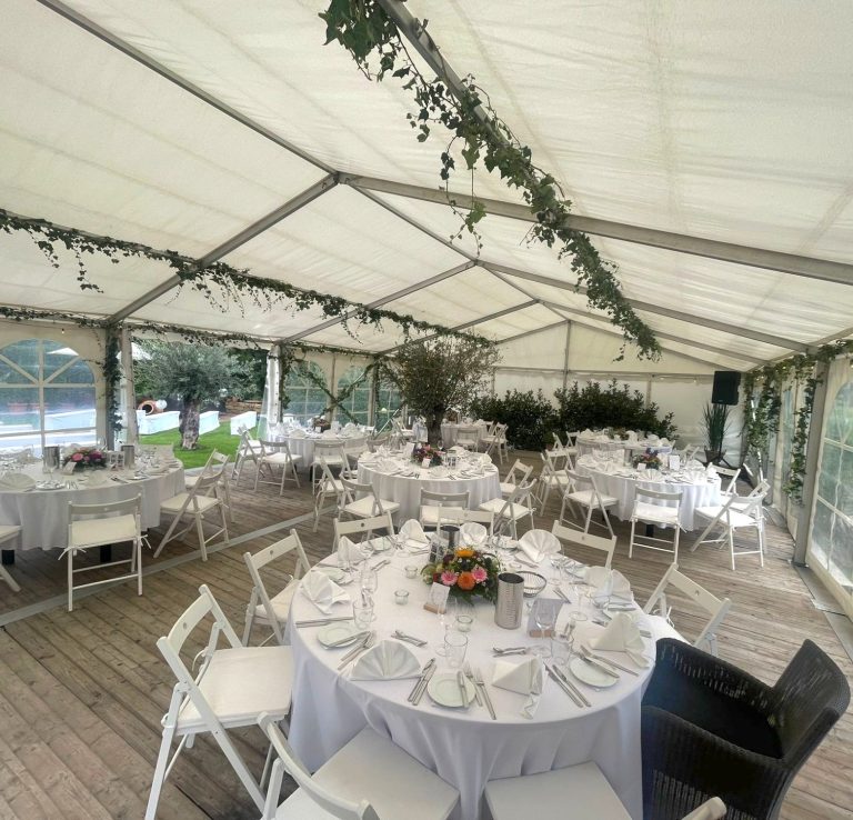 estlich gedeckter Tisch im Eventzelt Tischdeko in einem festlich gedeckten Zelt mit weißen Stühlen und Blumenarrangements.