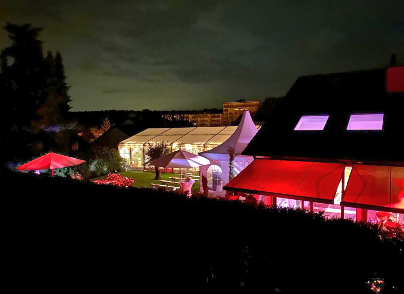 Hochzeitszelt mit Pagodenzelt Beleuchteter Außenbereich eines Veranstaltungsorts bei Nacht mit Zelt und roten Lichtakzenten.