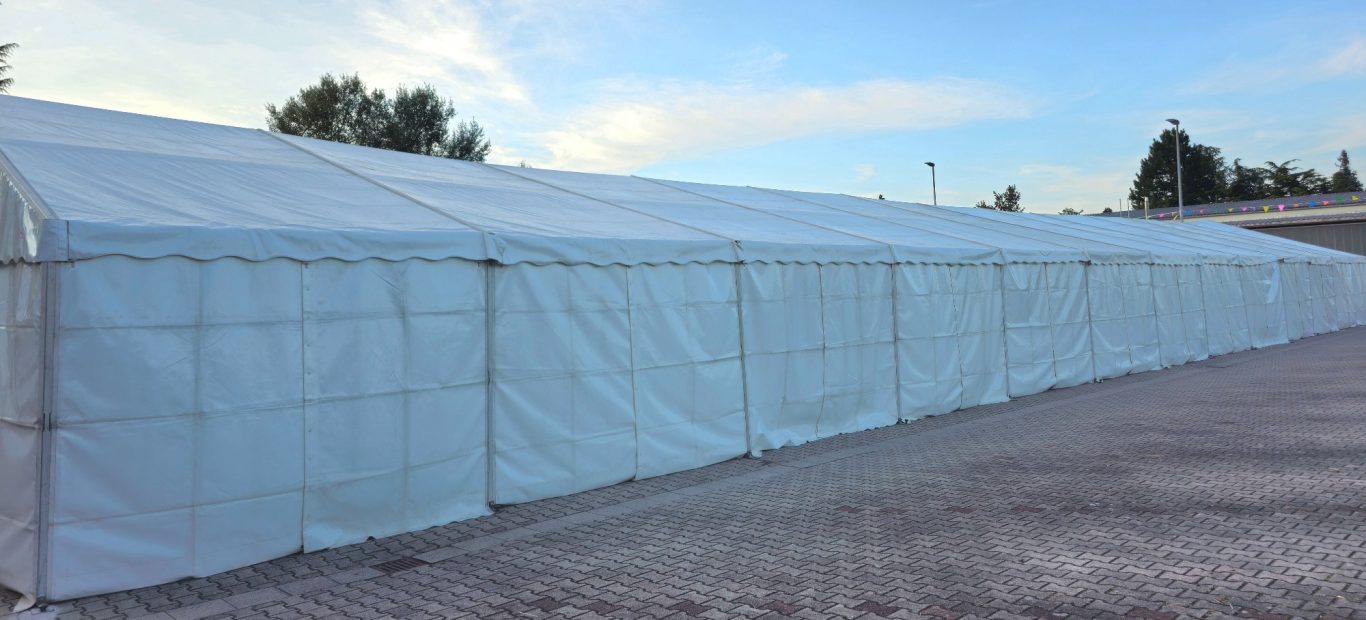 Temporäres Lagerzelt mit Seitenplanen Weiße Zeltkonstruktion auf einem gepflasterten Platz, mit blauem Himmel im Hintergrund.