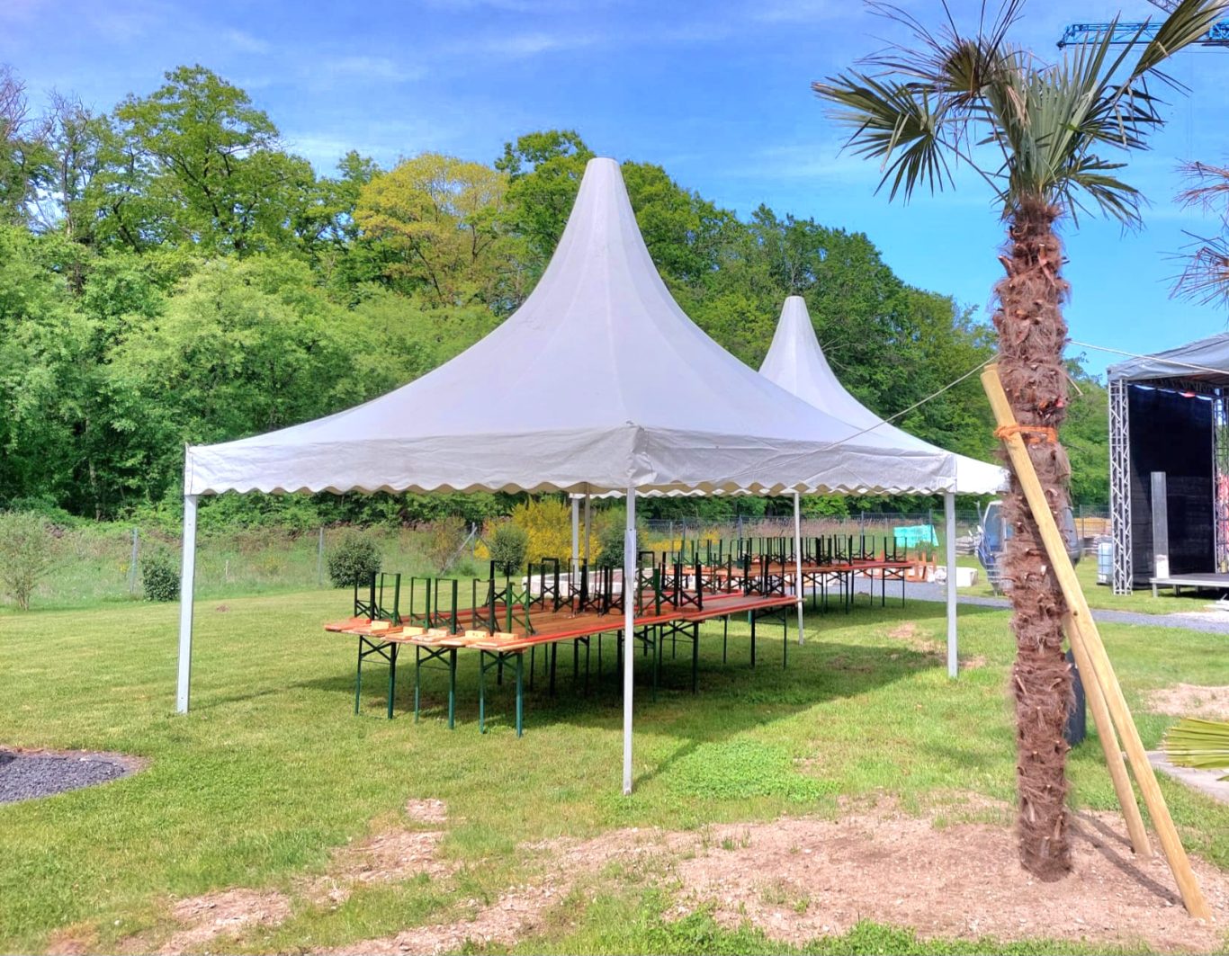 Pagodenzelt ohne Seitenwände Weißes Partyzelt im Freien mit langen Tischen, umgeben von grünem Gras und Bäumen.