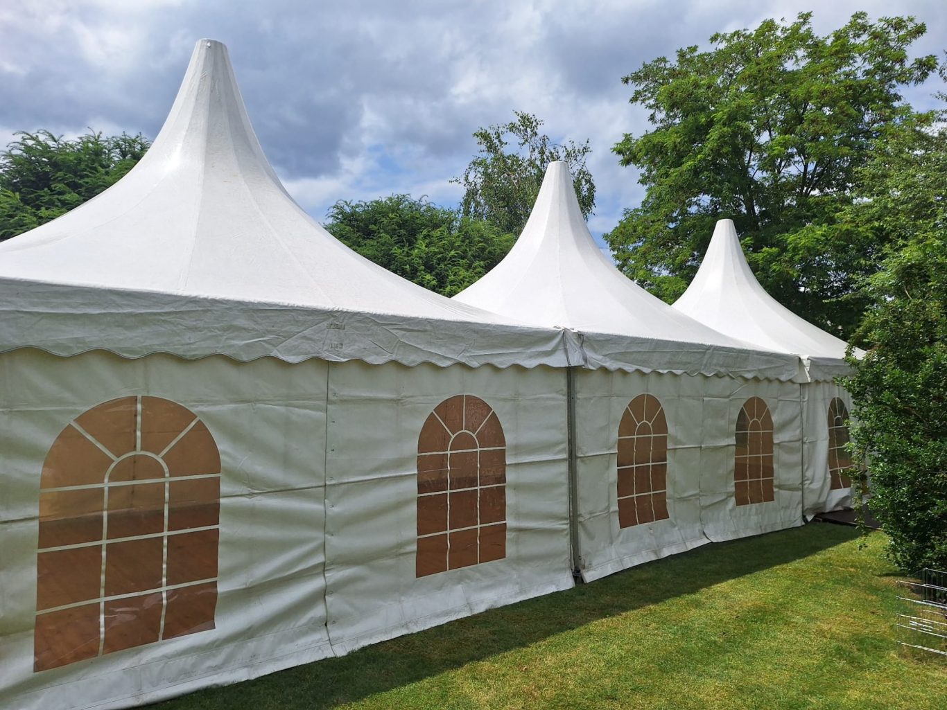 Drei Pagoden verbunden im Garten Zelt mit spitzen Dächern und Fensteröffnungen, umgeben von Grünflächen.