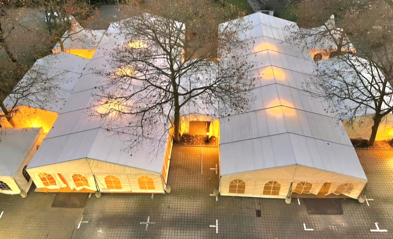 Zwei 10m Zelte verbunden mit 4m Zelten Zwei festliche Zelte mit Beleuchtung, umgeben von Bäumen und einem Parkplatz.