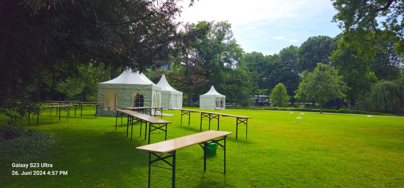 Pagodenzelte verschiedener Größen im Zoo Drei Pagodenzelte stehen auf einer grünen Wiese im Zoo, umgeben von Bäumen und Tischen.