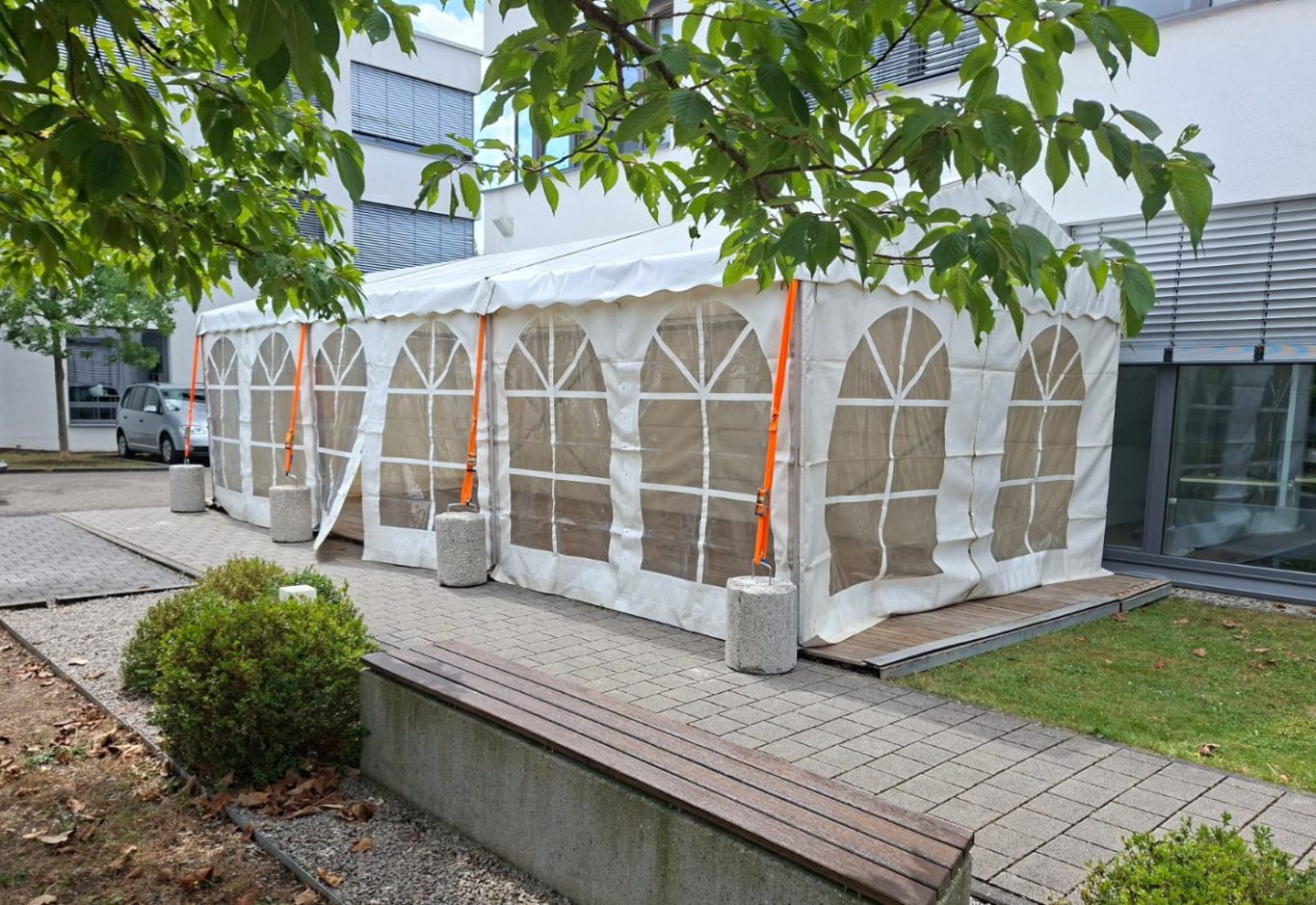 4m breites Zelt mit Fenstern Ein 4m breites, weißes Zelt mit Fenstern, umgeben von Bäumen und einem Gehweg.