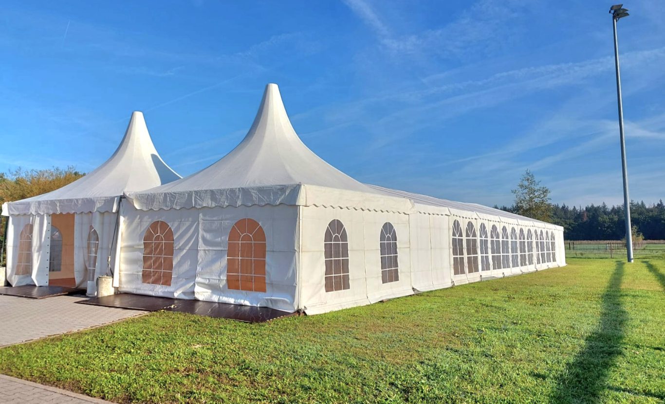 Pagodenzelte auf Reiterhof im Verbund Zelt mit spitzen Dächern, weißen Wänden und großen Fenstern auf einer Wiese.