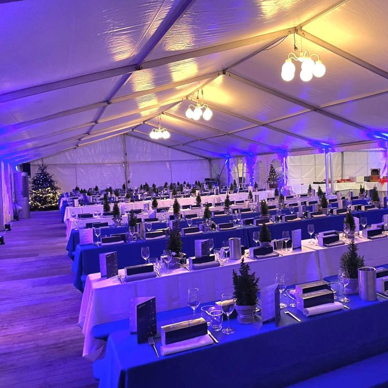 10m breites Festzelt mit Anbau und Zubehör 10m breites Festzelt mit Anbau und blauen Tischdecken, festlicher Dekoration und Beleuchtung.