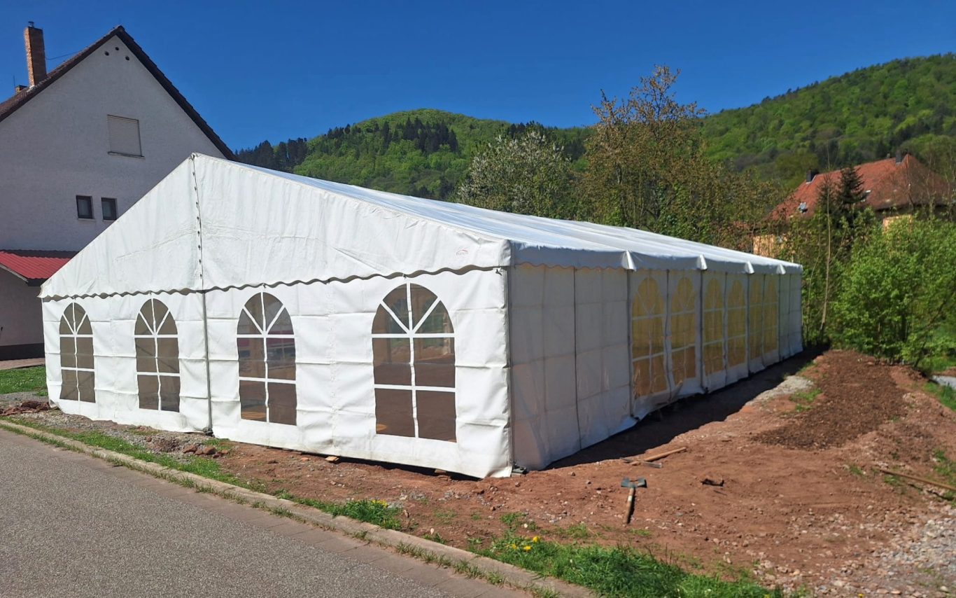 Großes weißes Partyzelt Großes, weißes Partyzelt mit Rundbogenfenstern, umgeben von Grünflächen.