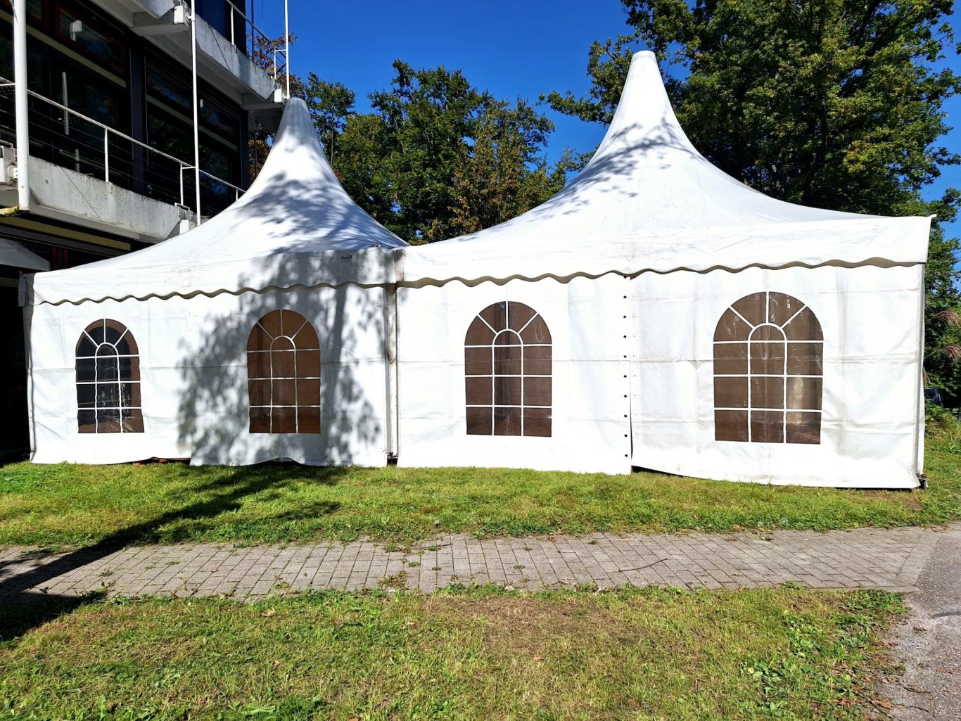 Pagodenzelte Weiße Zelte mit Spitzdächern und Fenster, auf einer grünen Wiese.