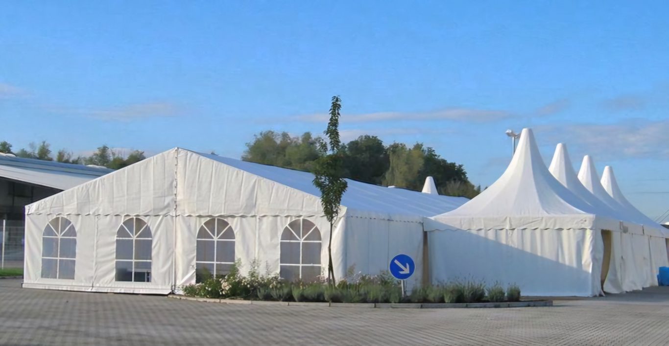 10m Zelt mit Pagodenzelt im Verbund Weißes Festzelt mit spitzen Dächern und großen Fenstern auf einem Platz.