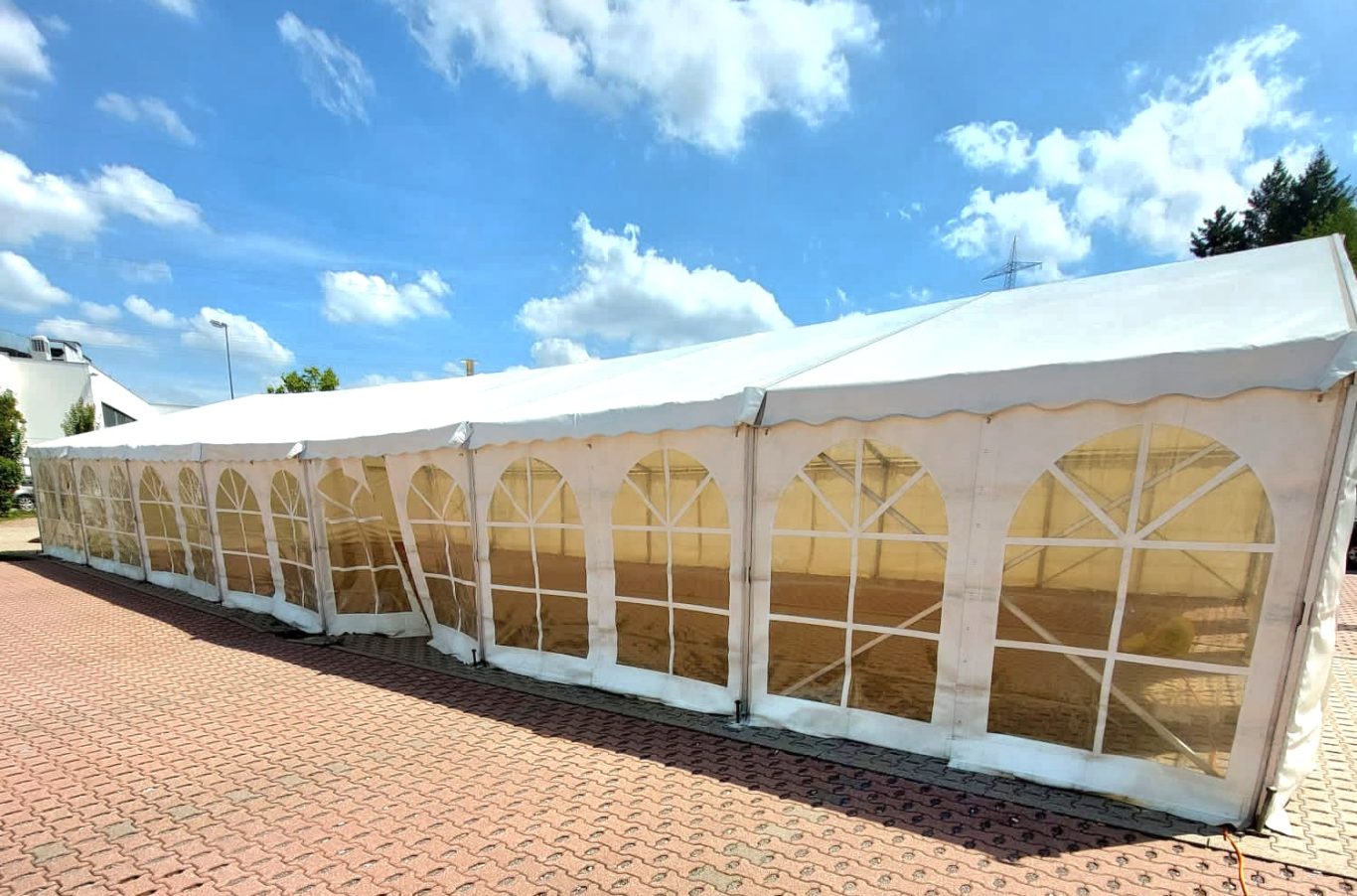 8m breites Zelt mit Fenstern Weißes Zelt mit Seitenwänden und Fenstern, unter blauem Himmel.