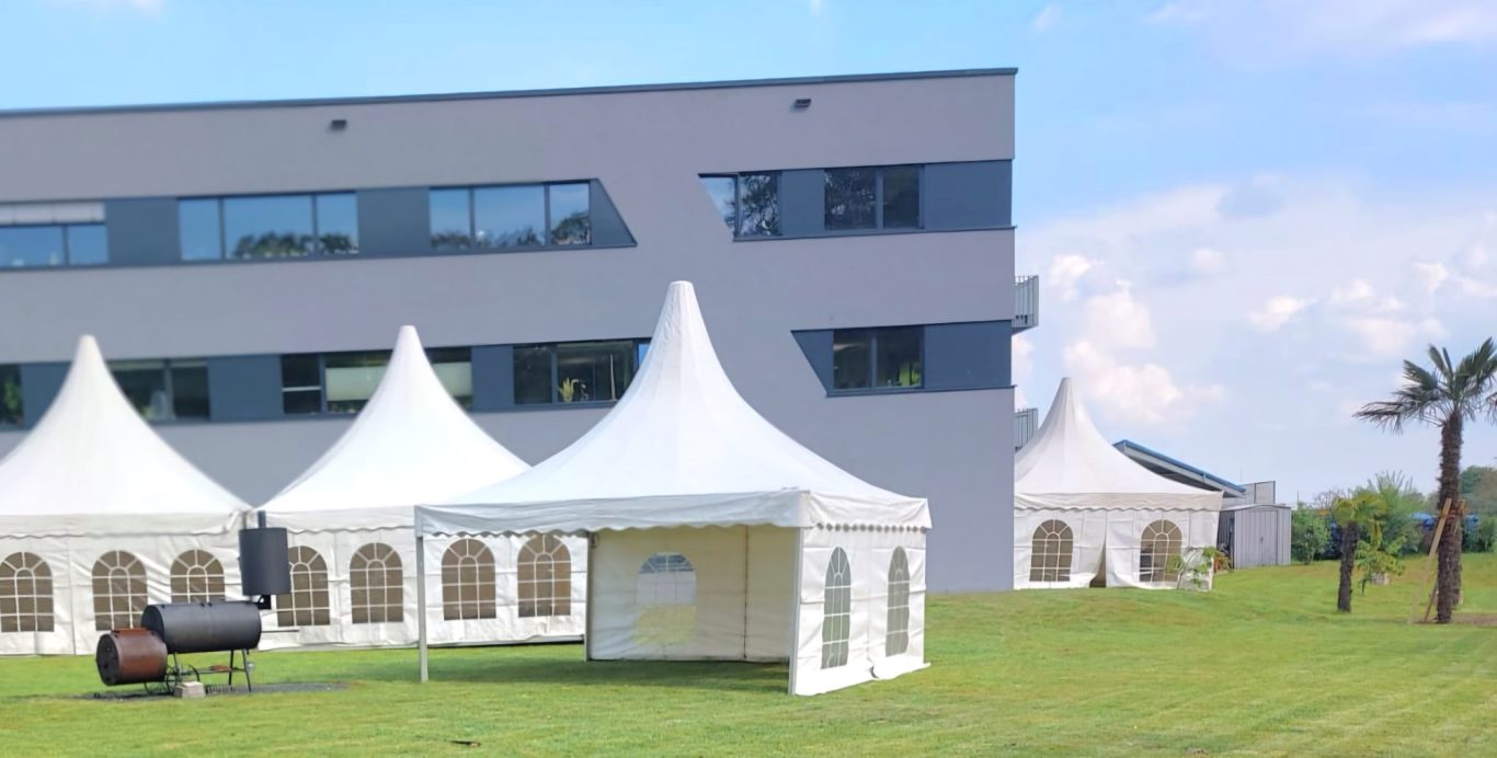 Pagodenzelte für Firmenevent Zelte auf einer Wiese vor einem modernen Gebäude, sonniger Himmel.